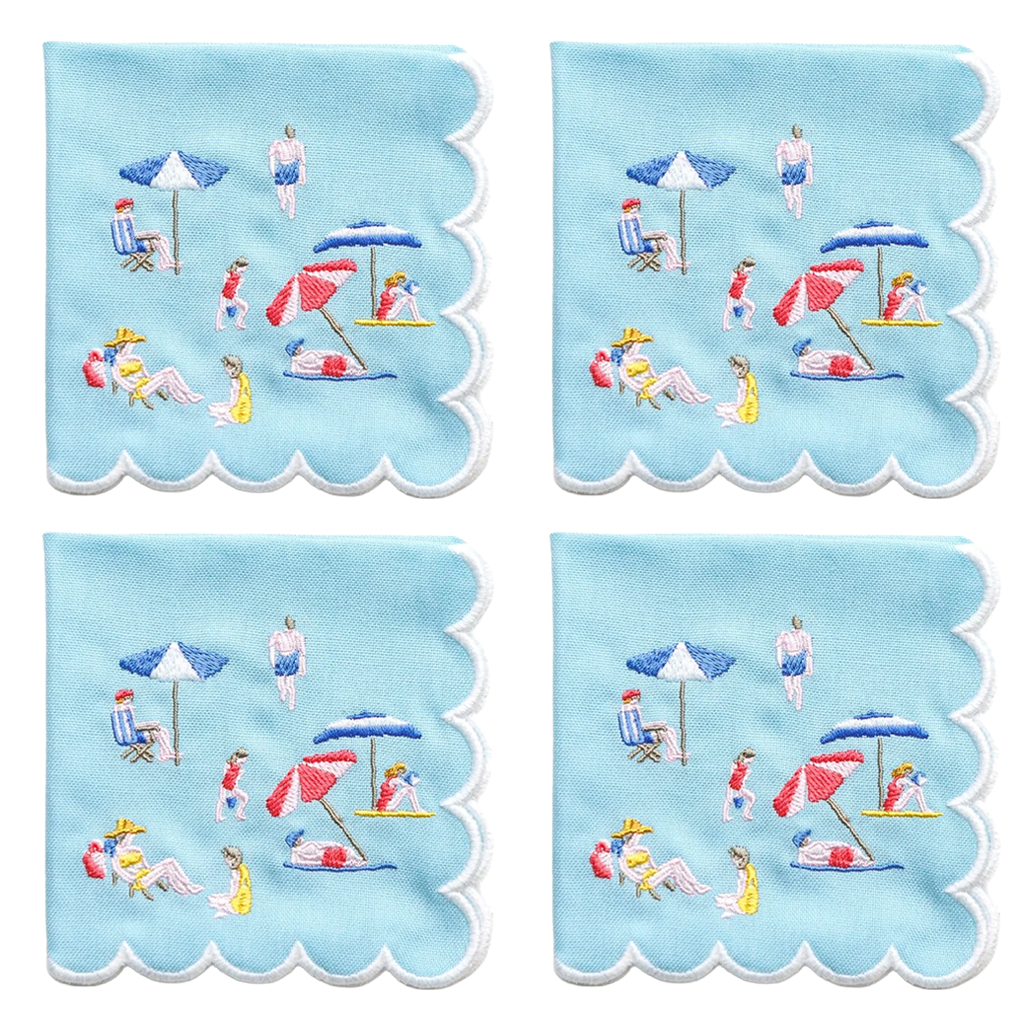 Four square light blue napkins with scalloped edges, each printed with a beach scene featuring people, umbrellas, chairs, and towels in small multicolor embroidery.