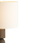 Close-up of a table lamp with a warm white fabric drum shade and a dark wood base, shown against a plain white background.