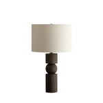 A modern table lamp with a dark brown wood base featuring stacked cylindrical and spherical elements, topped with a large off-white fabric drum shade, shown on a plain white background.