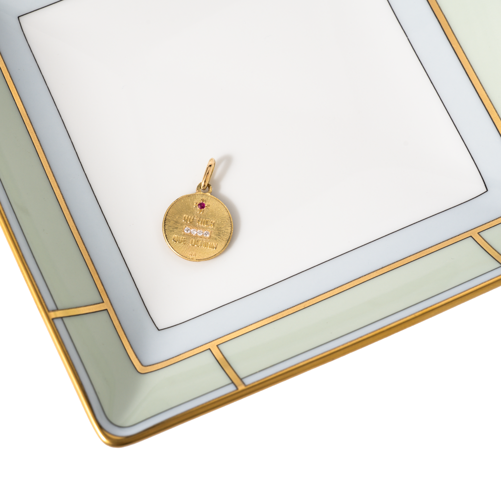 Gold pendant with a red gemstone on a white card with gold border