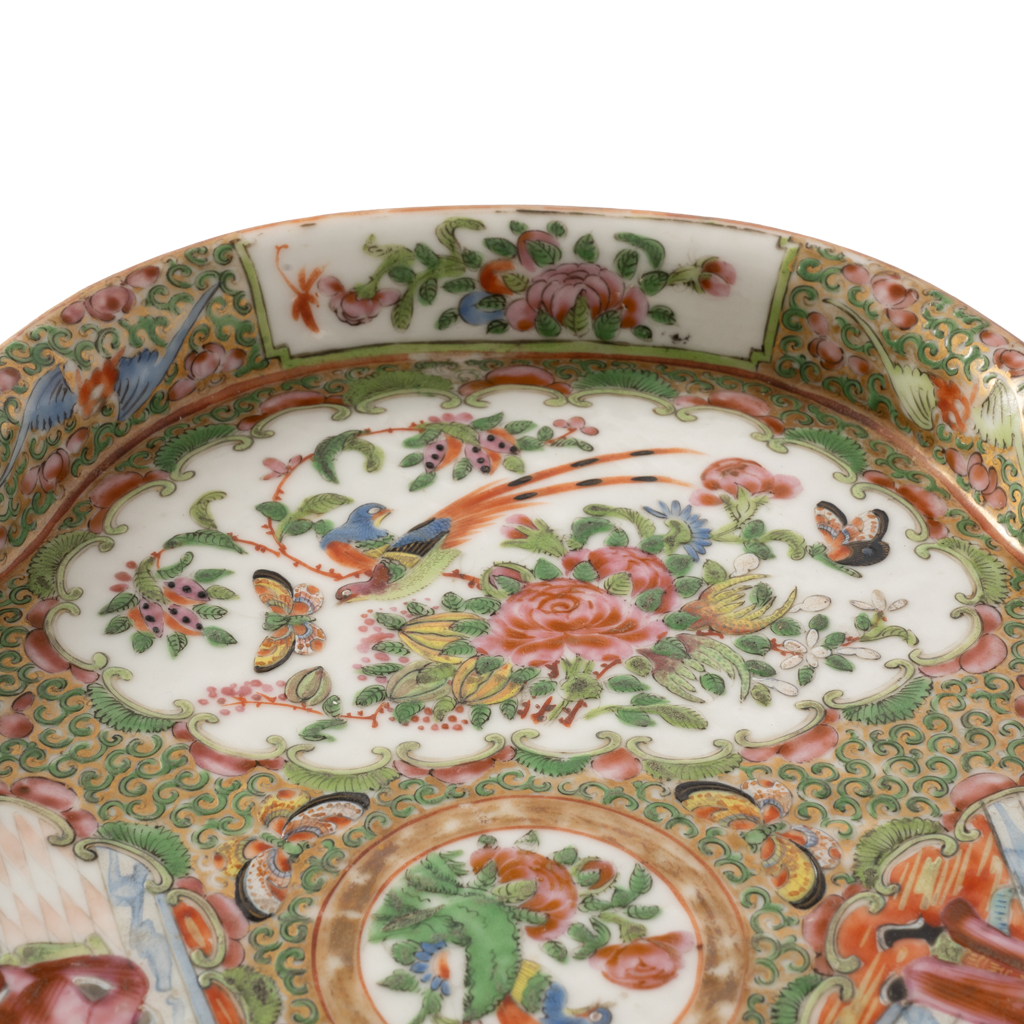 Close-up of an ornate porcelain plate with a white ground and intricate hand-painted floral and bird motifs in green, pink, orange, blue, and yellow.