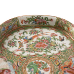 Close-up of an ornate porcelain plate with a white ground and intricate hand-painted floral and bird motifs in green, pink, orange, blue, and yellow.