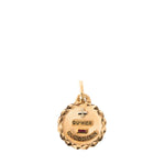 A gold-toned round pendant charm with a faceted textured edge, featuring a small cross at the top, the engraved words 'QU'HIER' and 'QUE DEMAIN' on either side of a small red ruby detail, and a bail at the top for a chain.