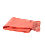 A folded coral orange throw blanket with fringed edges and a small dark logo tag, shown on a plain white background.
