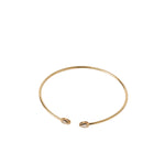 A thin gold open cuff bangle bracelet with a small oval charm at each end, shown on a plain white background.
