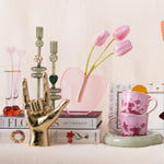 Decorative setup with a gold hand sculpture, pink tulips, and floral mugs on a shelf.