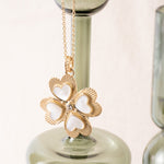 Gold necklace with a clover-shaped pendant on a reflective surface