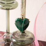Green heart-shaped pendant on a chain with a glass candle holder in the background
