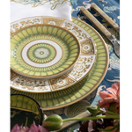 Decorative green and gold plate on a table with flowers and cutlery