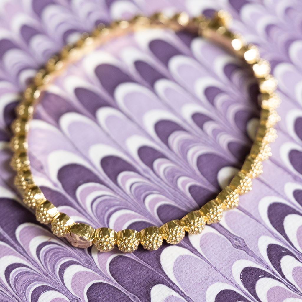 Gold beaded bracelet on a purple patterned background