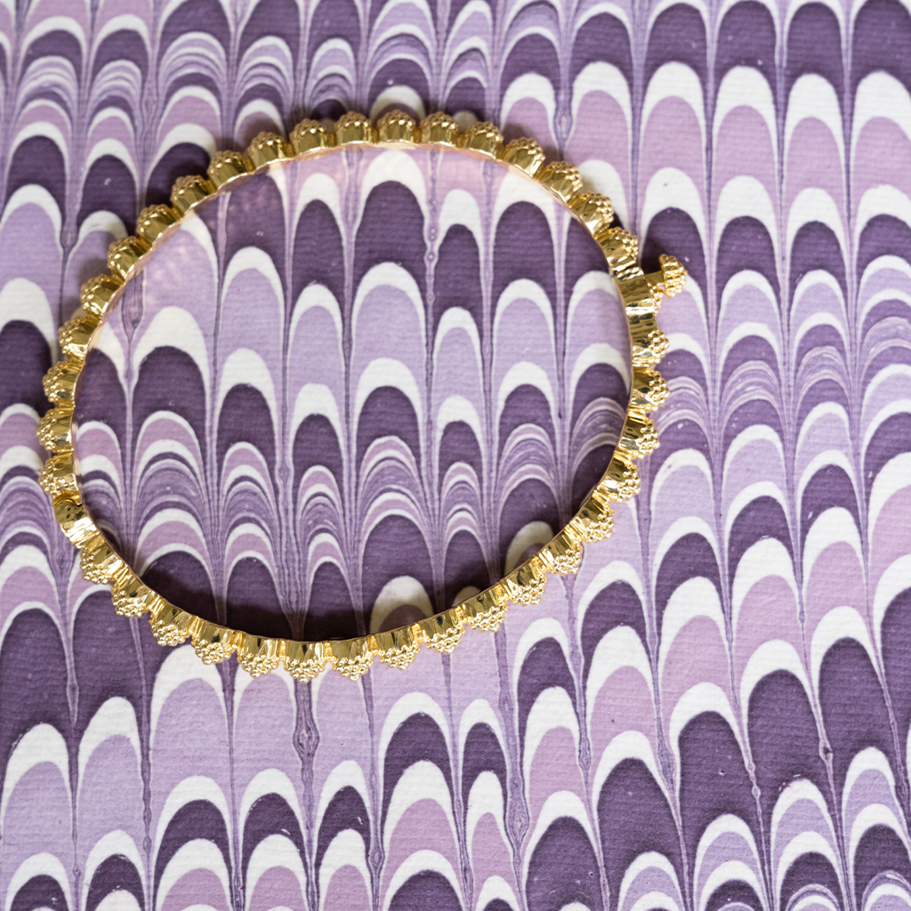 Decorative gold bangle on a purple and white patterned background