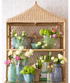 Wicker shelf with various vases and flower arrangements against a light background