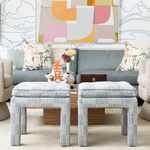 Living room with gray sofa, patterned ottomans, and colorful abstract art on the wall.