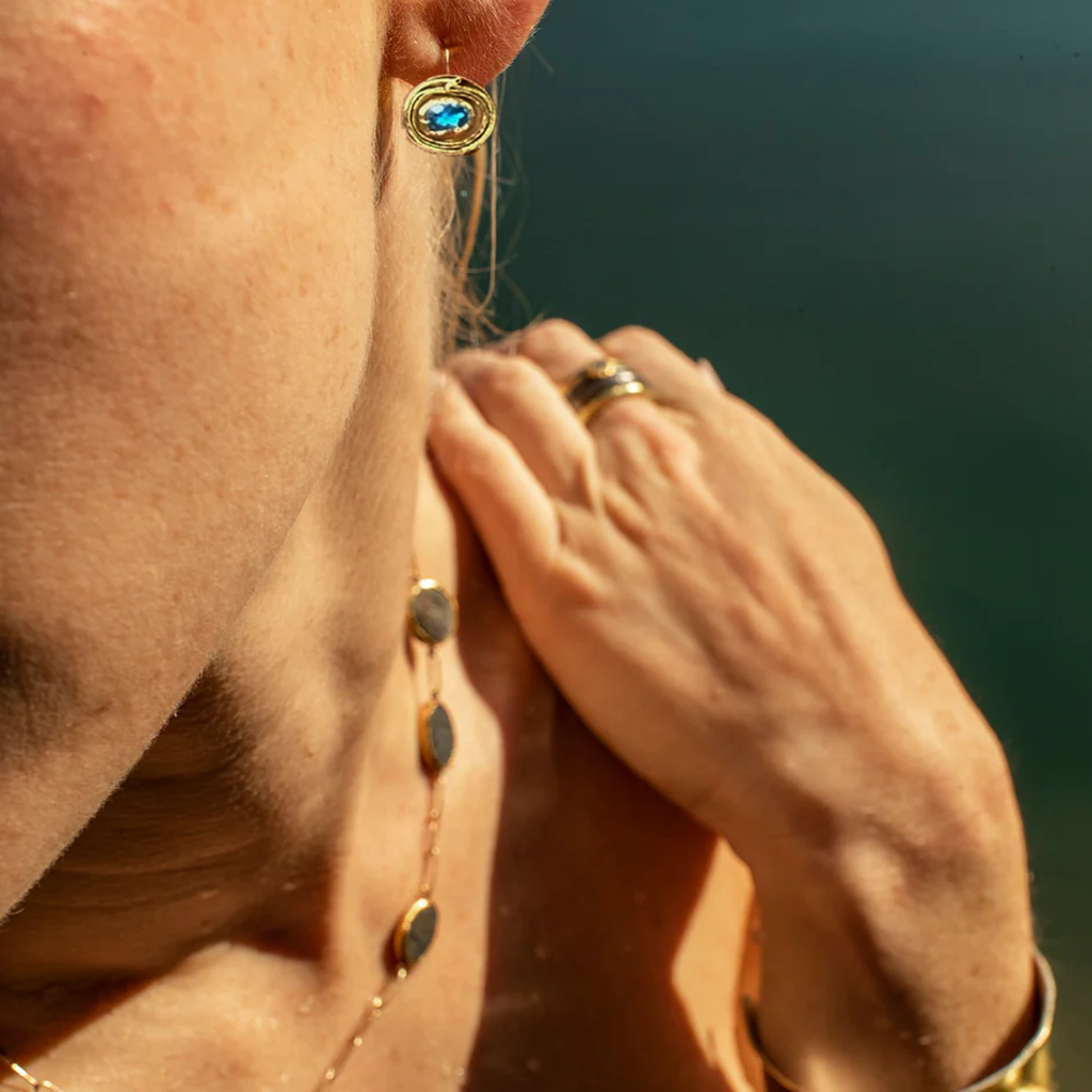 Close-up of a person wearing gold earrings and a ring with a blurred natural background