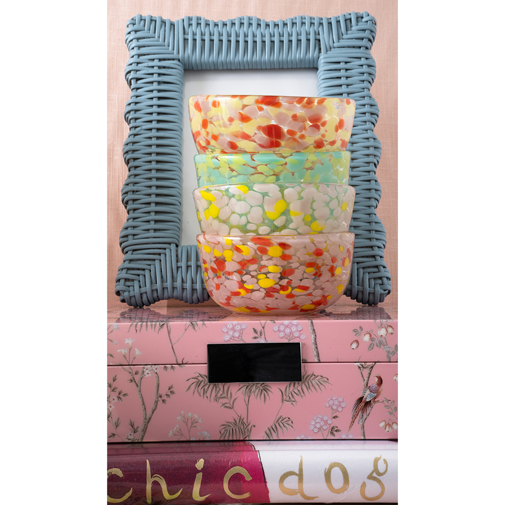 Decorative stack of colorful bowls with a textured blue frame on a pink surface.
