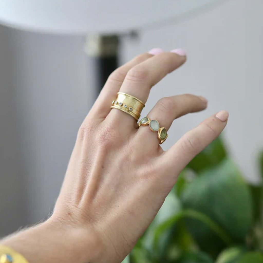 Hand wearing multiple gold rings with gemstones against a blurred indoor background