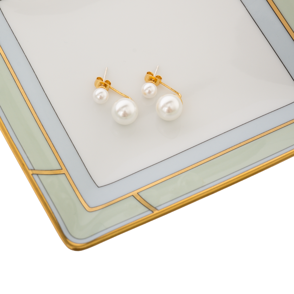 Pearl earrings on a decorative tray with a gold and white design