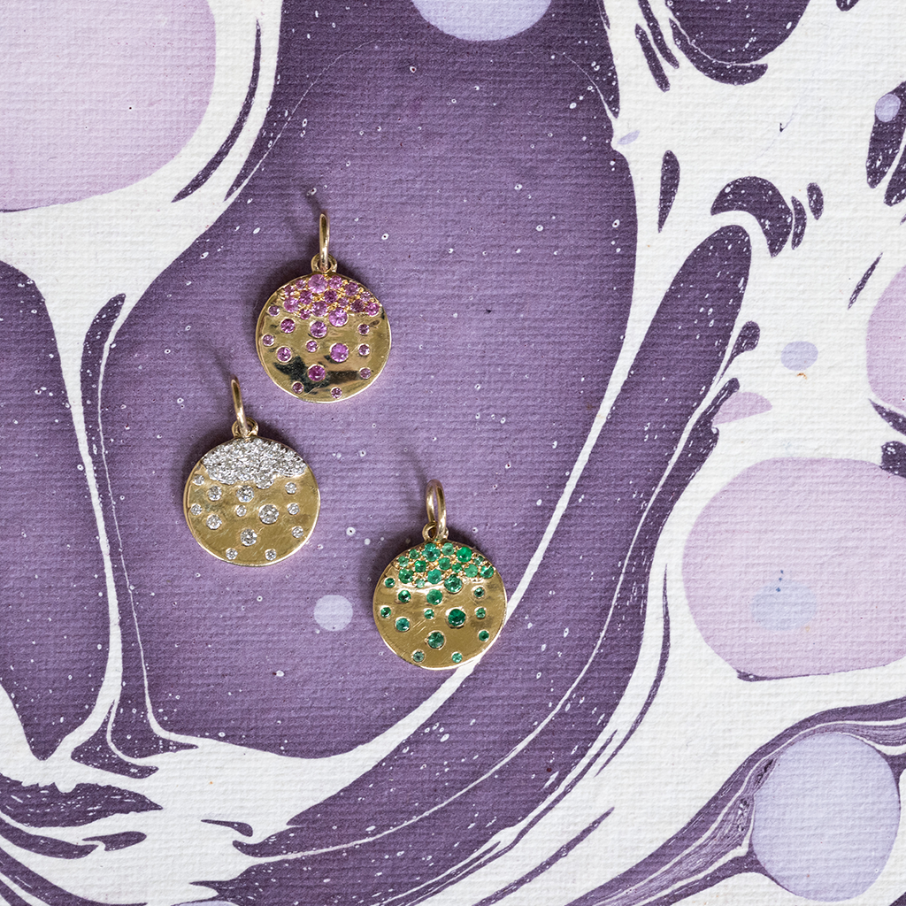 Three gold pendants with gemstones on a purple and white marbled background