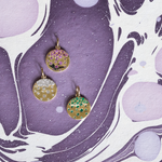 Three gold pendants with gemstones on a purple and white marbled background
