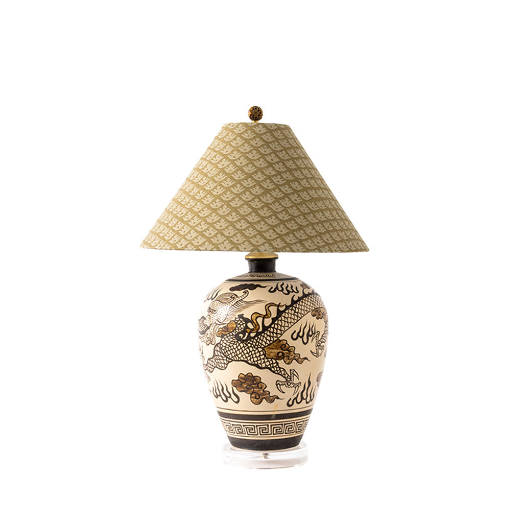 A table lamp with a beige patterned fabric shade and a cream ceramic base decorated with a black dragon motif, shown on a plain white background.