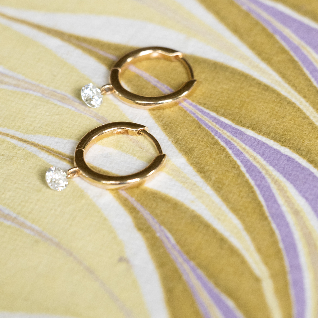 Gold hoop earrings with clear gemstones on a yellow fabric background