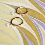 Gold hoop earrings with clear gemstones on a yellow fabric background