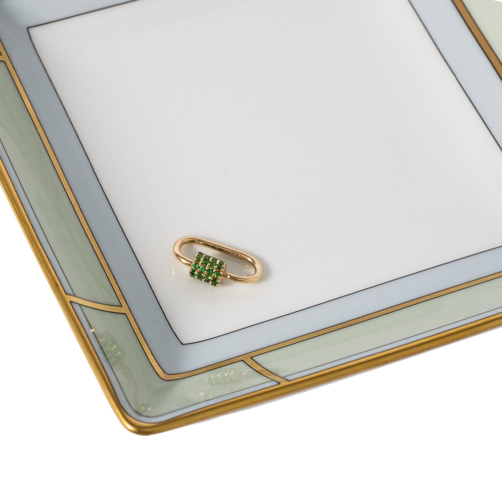 Gold charm with green gemstones on a white surface