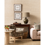 A styled living room corner featuring a beige textured wallpapered wall, a dark wood console table with a green ceramic lamp, two patterned armchairs, and framed bird artwork.