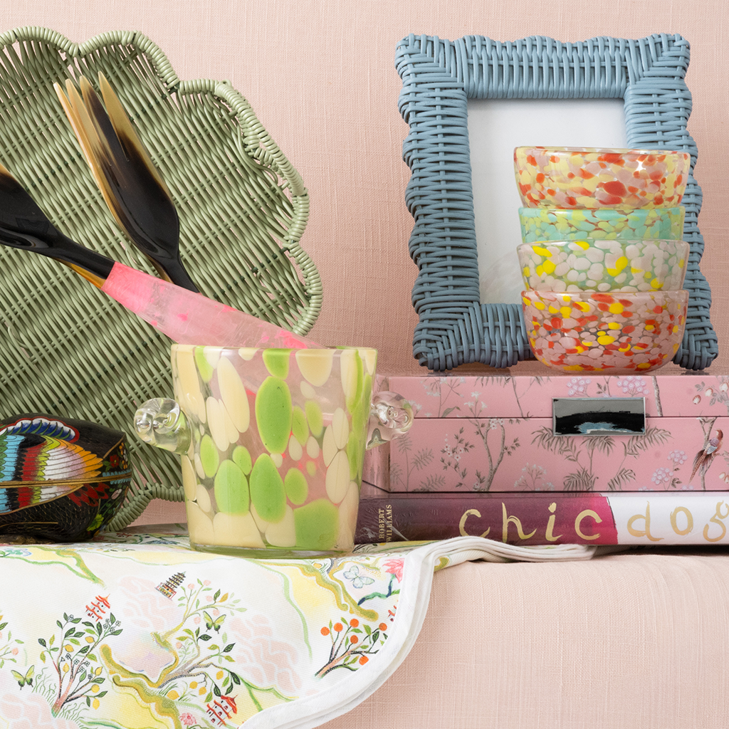 Decorative items including a green woven basket, colorful ice bucket, blue frame, and pink box on a pink surface.