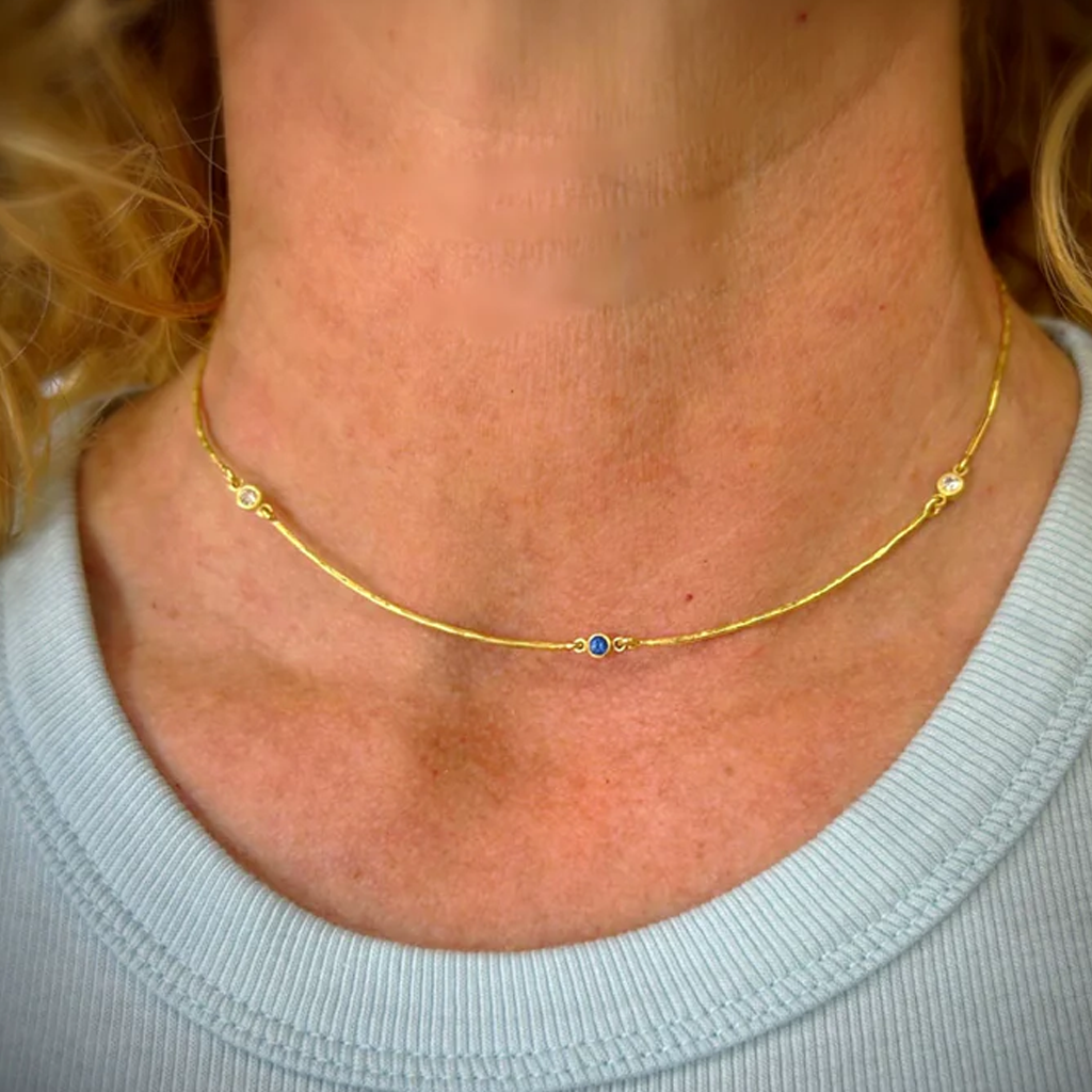 Gold necklace with blue gemstone and diamonds worn by a person