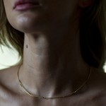 Close-up of a person wearing a gold necklace with a blurred background