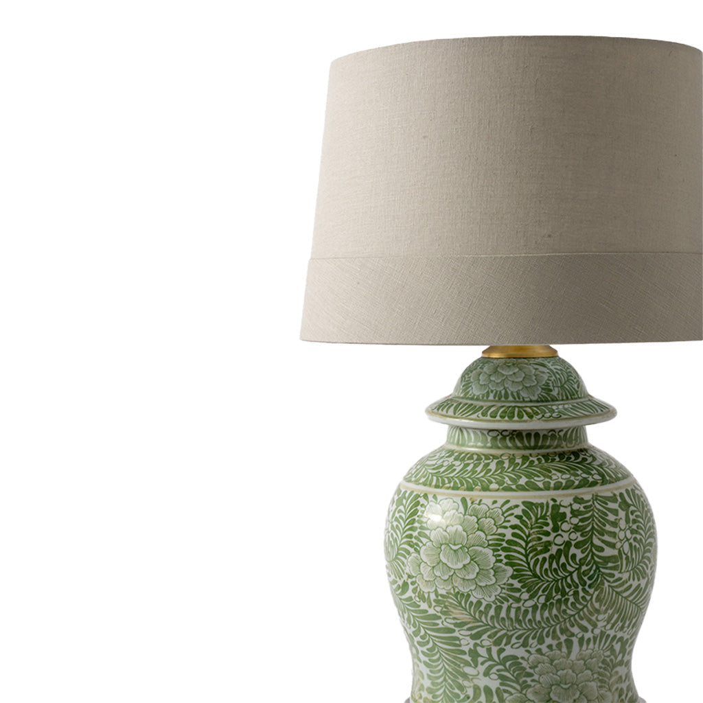 A table lamp with a green and white patterned ceramic base and a beige linen drum shade, shown against a plain white background.