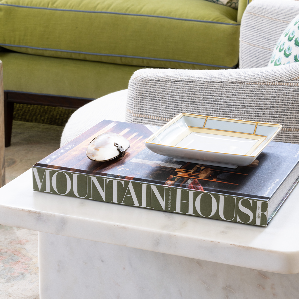 Book titled 'Mountain House' on a marble table with a decorative plate on top, in a living room setting.