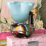Decorative goose with colorful patterns on a pink surface with books and a blue bowl.