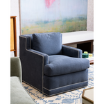 A dark blue swivel chair with white piping with artwork in the background