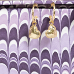 Gold heart-shaped earrings on a purple and white patterned background