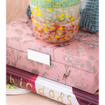 Stack of colorful books with a decorative pink box featuring floral patterns on a beige surface.