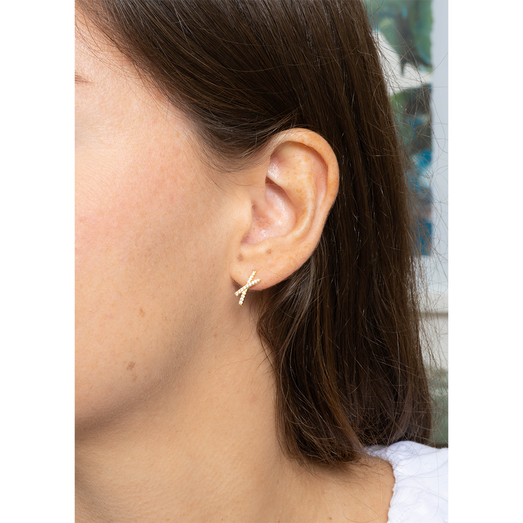 A close-up side view of a person's ear wearing a small gold-toned cross-shaped stud earring.