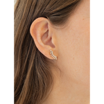 A close-up of a person's ear wearing a small gold leaf-shaped stud earring with clear stones.