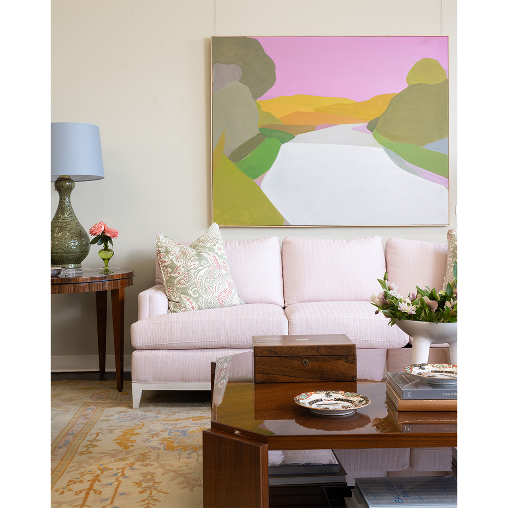 Living room with a pink sofa, wooden coffee table, and colorful abstract painting on the wall.