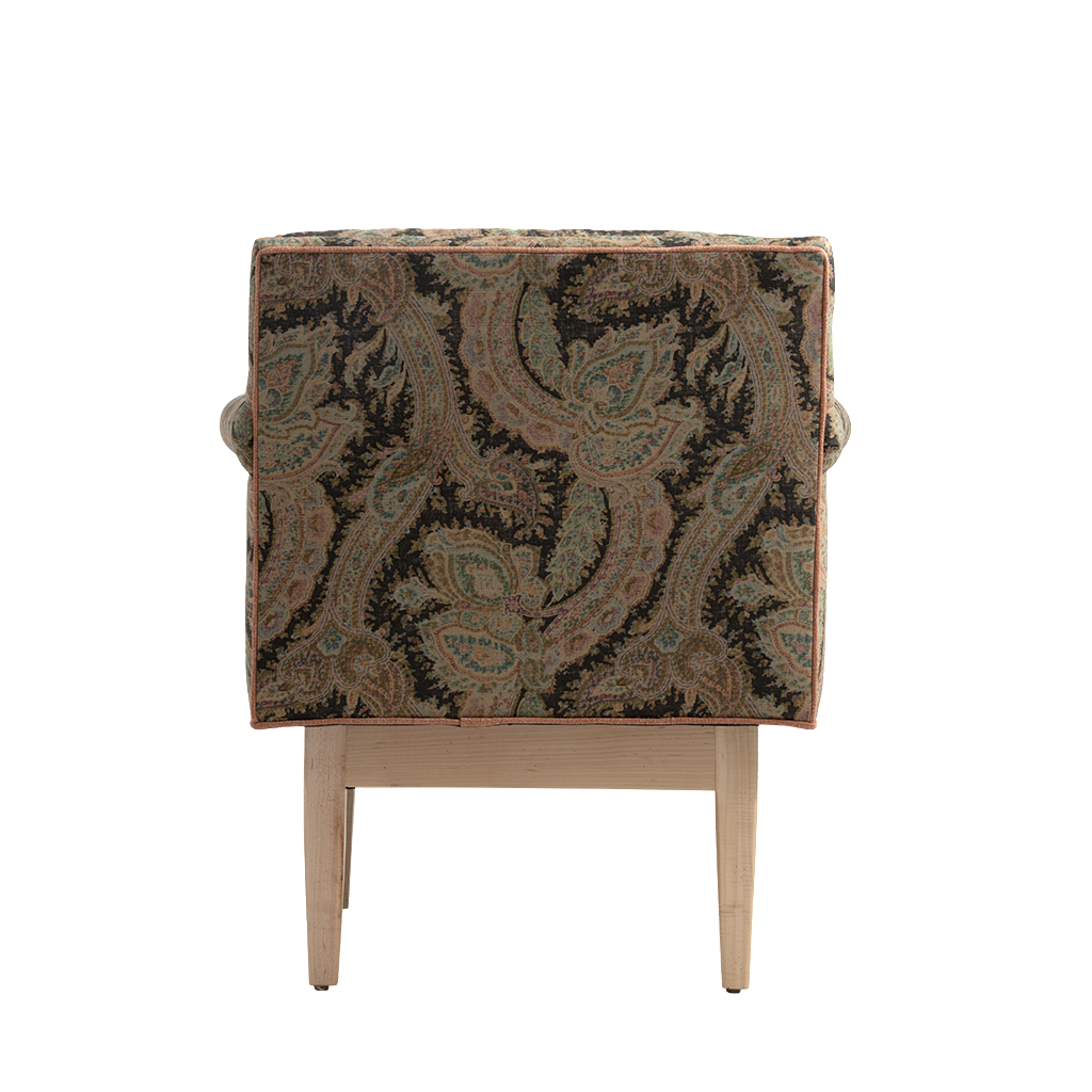 The back of a chair with a dark paisley patterned fabric in black, brown, and muted green, supported by a light natural wood frame with tapered legs.