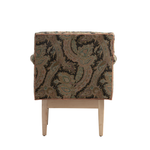 The back of a chair with a dark paisley patterned fabric in black, brown, and muted green, supported by a light natural wood frame with tapered legs.