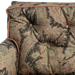 Close-up of a tufted armchair backrest and arm upholstered in an ornate paisley fabric with a rust-colored braided piping trim.