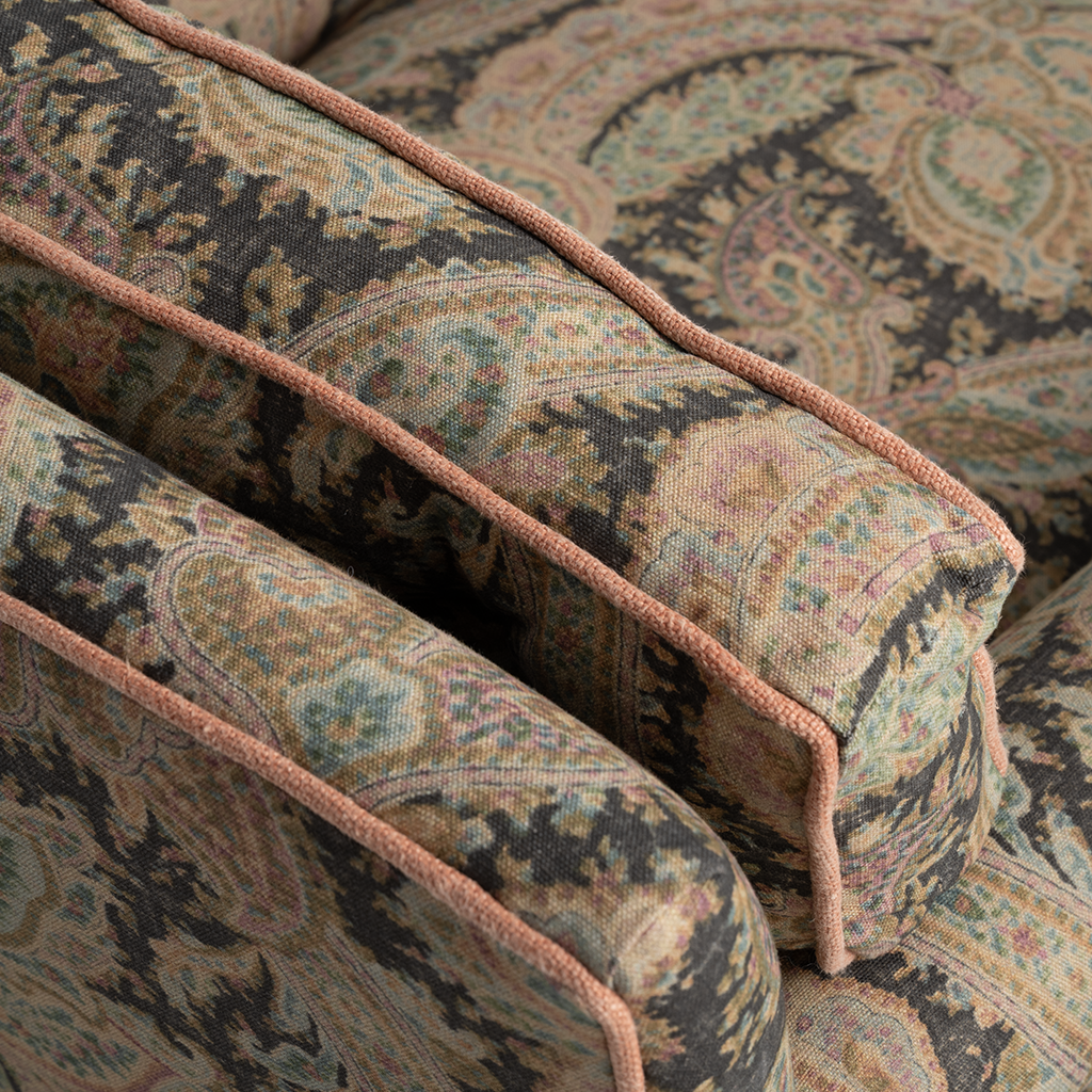 Close-up of upholstered armrests with a detailed paisley pattern in muted beige, brown, and teal tones, accented by a contrasting dusty rose pink piping.