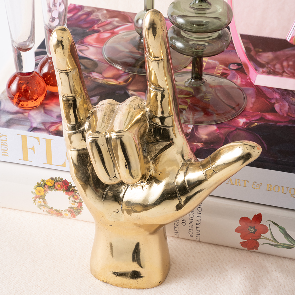 Gold hand sculpture making a love sign on a decorative surface with books and a glass.