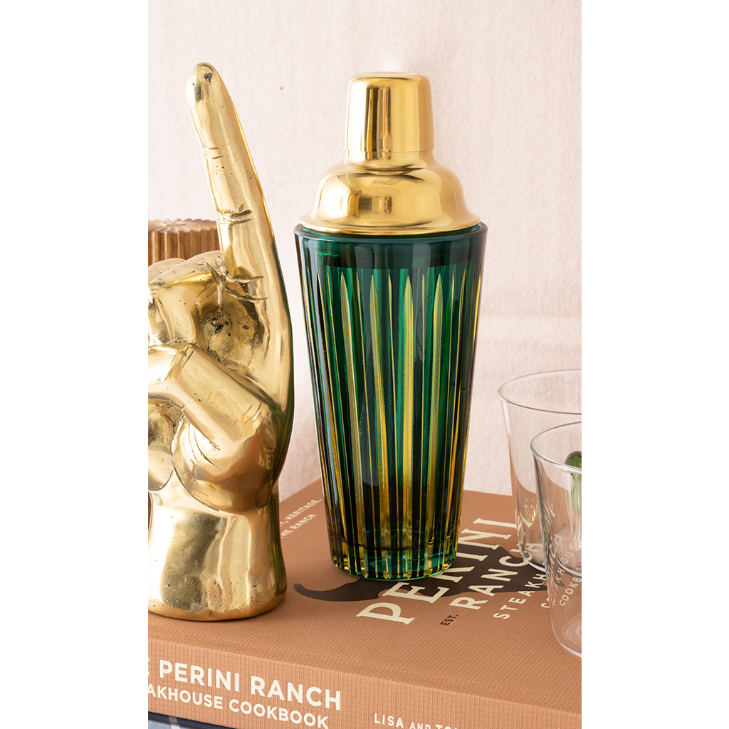 Gold cocktail shaker and book on a table with a neutral background