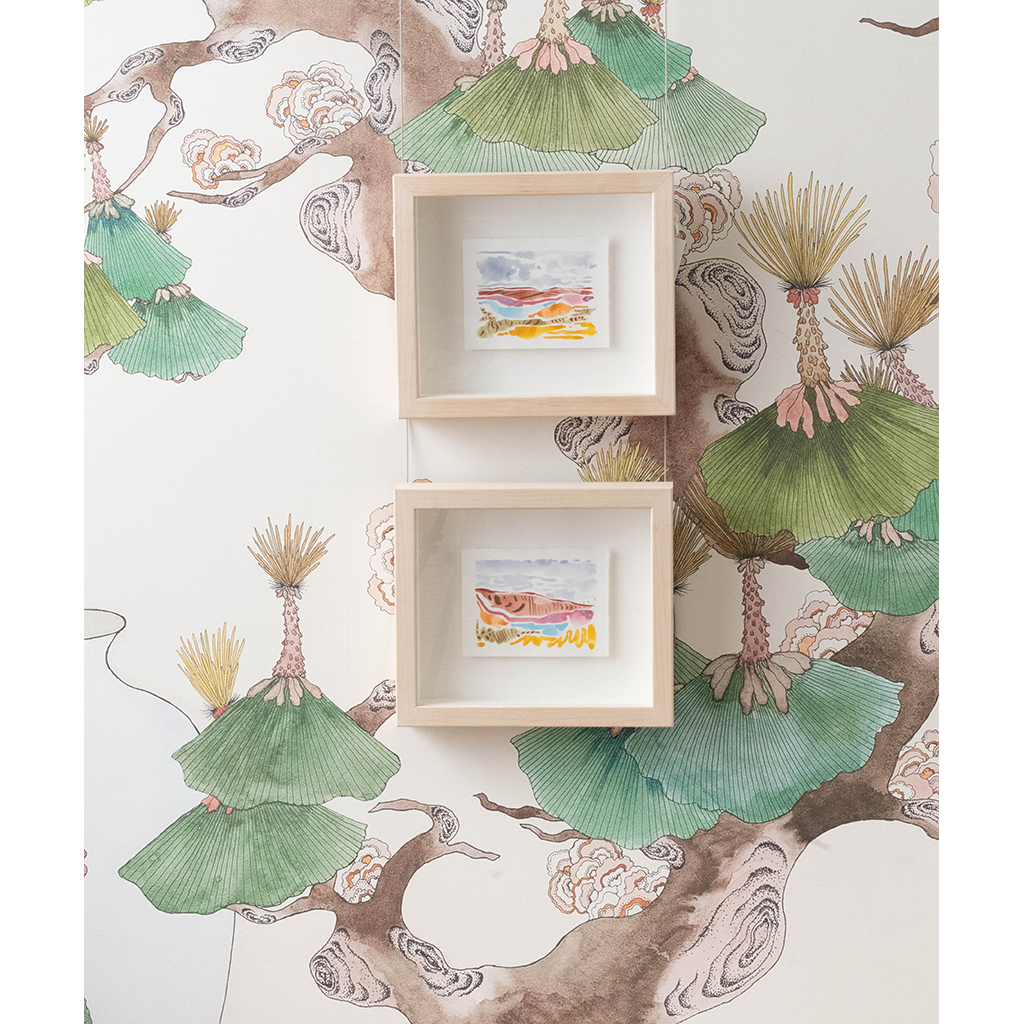 Two small framed watercolor art prints hang on a wall against a decorative wallpaper featuring green ginkgo leaves and brown tree branches.