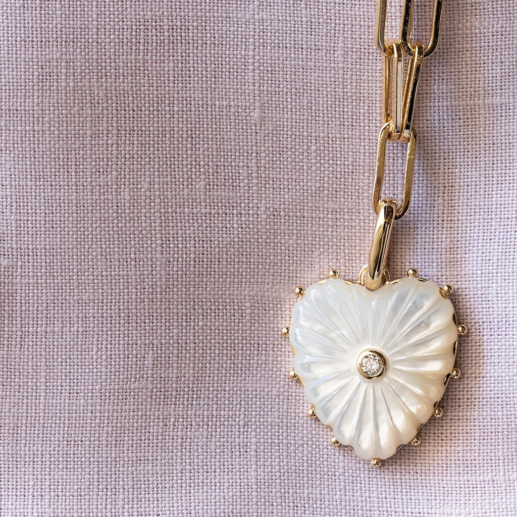 Heart-shaped pendant with a diamond on a gold chain against a textured beige background