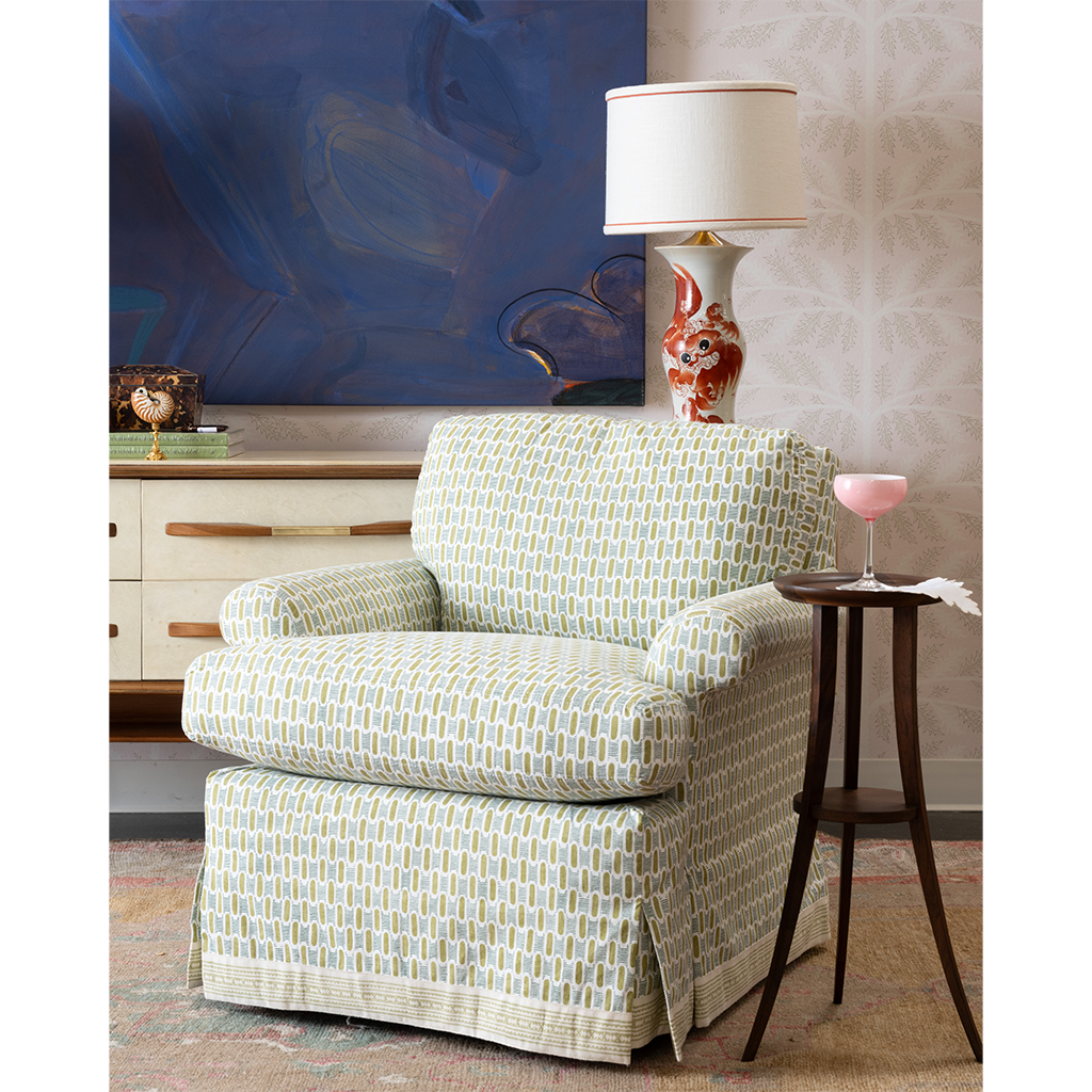 A green and blue chair and a wooden side table with artwork in the background