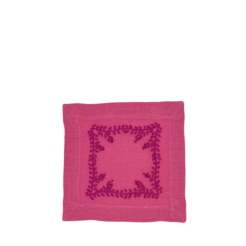 A square pink linen napkin featuring a dark magenta embroidered floral border design in the center, shown flat against a plain white background.